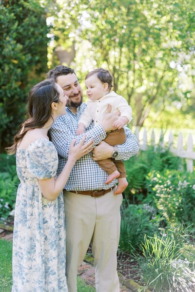 photo of a dad holding his baby while his wife looks on in a garden by richmond va family photographer jacqueline aimee portraits