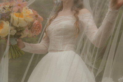 Whimsical bride under her veil holding a colorful bouquet
