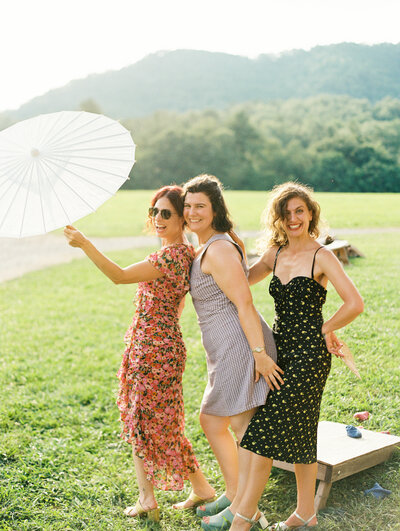 Wedding guests frolic in the sunlight with games and a parasol at the summer wedding at scenic North Carolina venue Paint Rock Farm, by destination photographer My Sun and Stars Co.