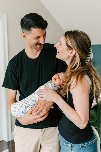 Couple standing in their Somerville home holding their newborn baby