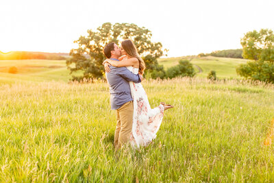 A white couple hugging each other closely and kissing in a grassy field