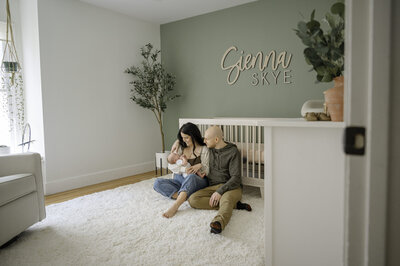 Parents sit on the floor of their daughters nursery while they hold and look lovingly at their newborn baby girl. Atlanta newborn photographer Amanda Touchstone