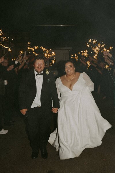 Bride and groom running through sparklers hand in hand
