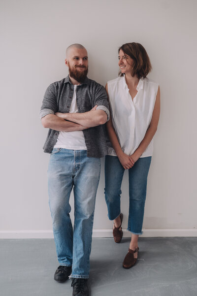 Marisa and Tanner of Msav Creative Co lean against a wall next to one another as they smile at each other