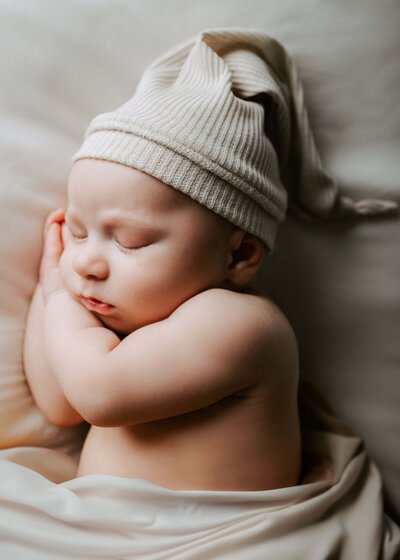 A newborn baby wearing a knitted hat peacefully sleeping on a bed, captured by a Pittsburgh newborn photographer.