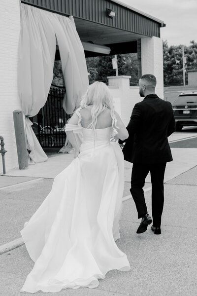A bride and groom walking hand in hand, entering the Grbic event reception venue.
