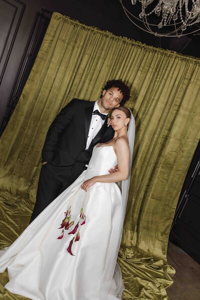 A bride and groom pose elegantly in front of olive-green drapery, showcasing luxury wedding photography in Montana with timeless and modern style.

