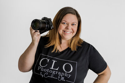 Photographer poses with her camera  and smiles in a Hampton Cover Alabama studio