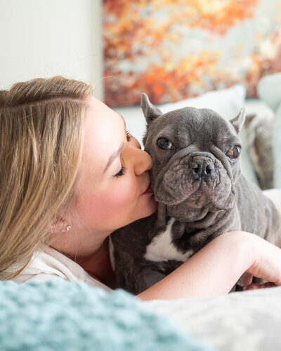 Woman snuggling a grey French Bulldog on a bed during an in-home pet photography session in Calgary