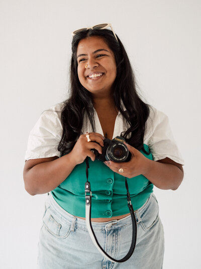 Portrait of Neha, the owner of Jeevan Portraits Photography smiling with sunglasses on her head holding her camera