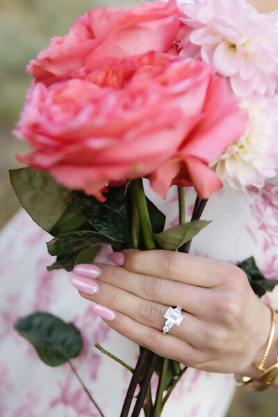 A close up of an engagement ring with some pretty pink flowers, photo taken by Kelly Elizabeth Photography.
