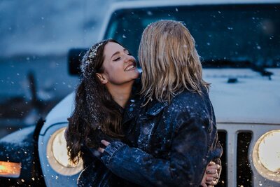 LGBTQ+ couple embraces during snowy winter engagement session.