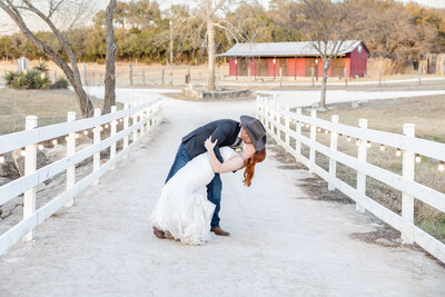 bride and groom kiss white fence red barn wedding in Boerne Texas by Firefly Photography