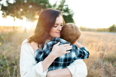 Mother lovingly hugs her young son during an outdoor family session with Jennifer L. Kirk Photography in Allen, Texas. Capturing authentic, heartfelt motherhood portraits in natural light.