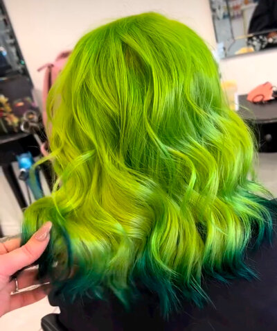 Image of client with hair that has been dyed a bright, vivid green with dark green lowlights.