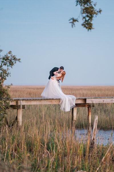 A newly wed couple kissing on a bride over the intercoastal waterways in Beaufort at sunset by destination wedding photographer, JoLym Photography