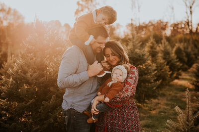 Family photoshoot with family posing in front of evergreen trees during golden hour