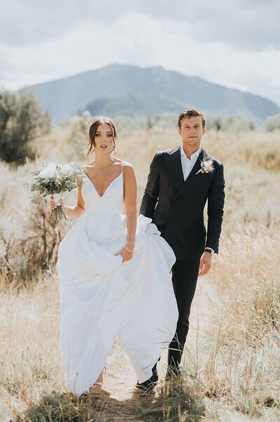 a Colorado wedding photography couple in Aspen walking through a field with a mountain backdrop behind them