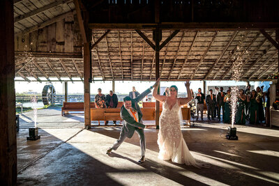 A newlywed couple makes a joyful grand entrance at The Barn by Fernbridge, greeted by cheering guests in a beautifully lit rustic barn wedding reception in Northern California.