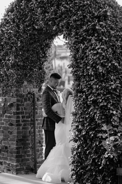 black and white photo of bride and groom beneath ivy growing