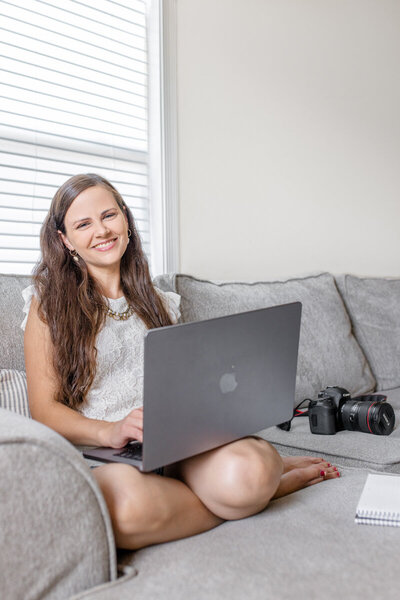 Robin sitting on a couch with a laptop and her camera sitting nearby