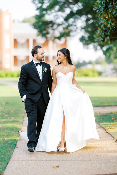 bride and groom wearing ballgown white gown and black tux walk together down pathway