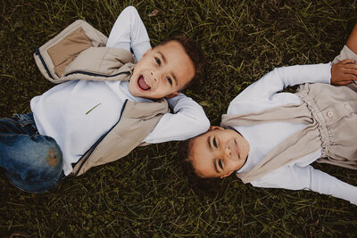 Two small kids laying opposite directions in the grass 