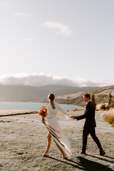 The Lovers Elopement Co - bride and groom walk outside Jack's Point Queenstown wedding venue at wedding elopement