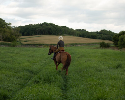 Sasha riding brown horse through grassy field on the farm in Chicago