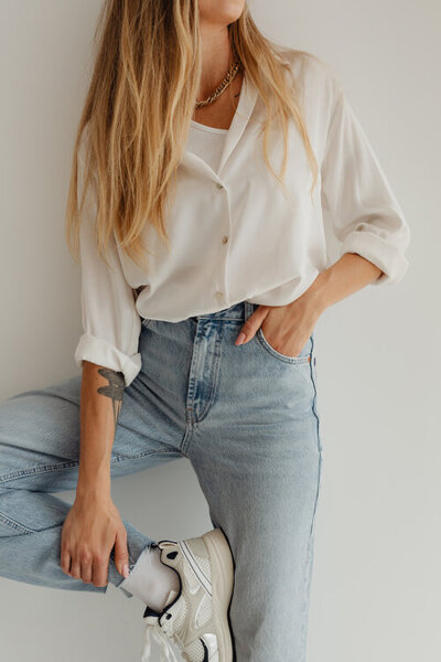 žena v bílé košili a džínách se opírá o zeď