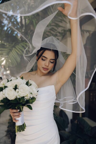 bride lifts up veil and holds bouquet