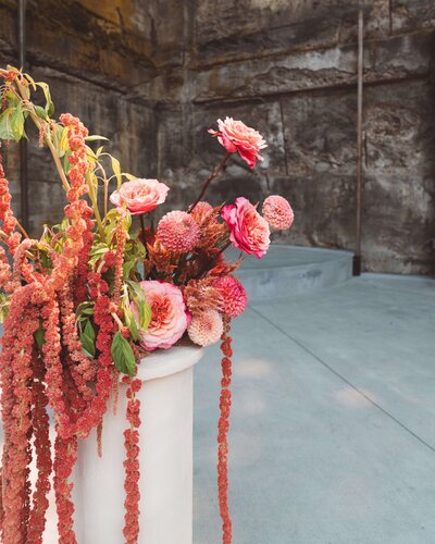 A candid wedding photo of a couple walking down the aisle after their ceremony. The groom is on the left wearing a white tuxedo jacket and black pants.  The bride is on the right and is wearing a semi sheer lace wedding dress. The bride is carrying a colorful wedding bouquet. The setting is at The Griffin House in Hood River, Oregon.