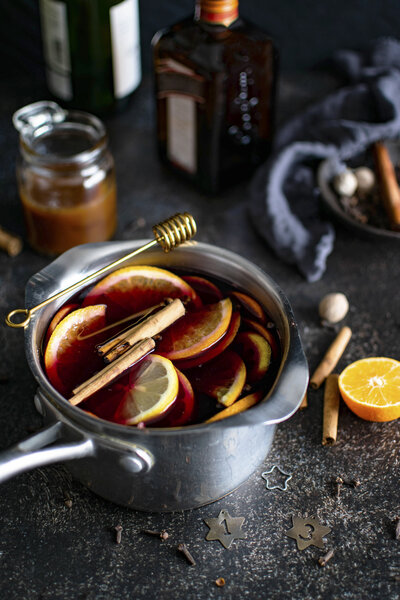 metal cup of mulled wine with orange and spices sitting on a counter with honey stick