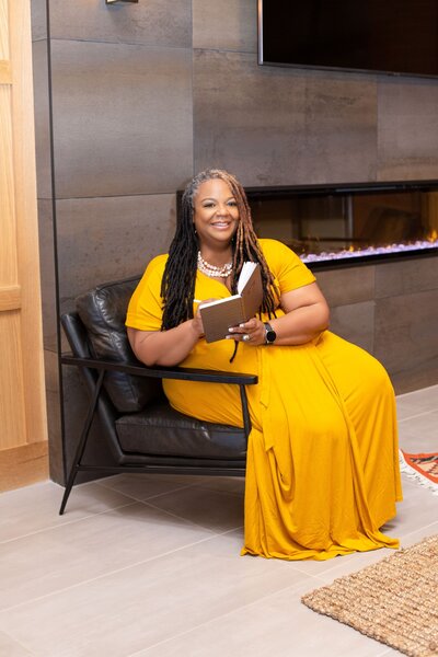 Kisha  standing at a table in black dress with book in her hand