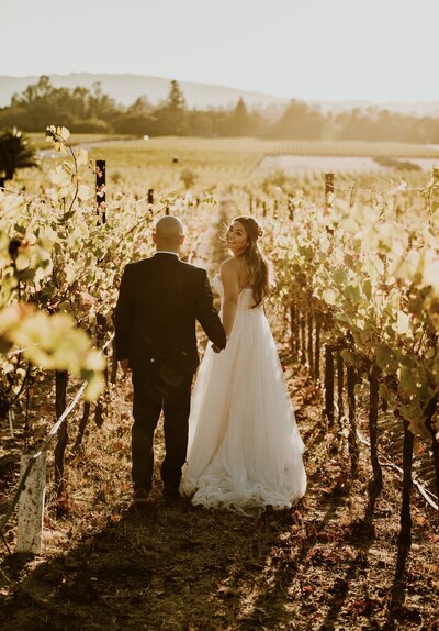 Couple walking together between vineyard rows at sunset after their elopement ceremony