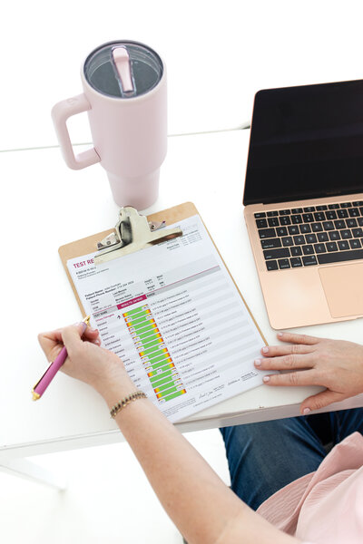 A women's health specialist at Reforme Wellness writes down details for a Discovery Visit using a pink pen, with her laptop on a white desk.