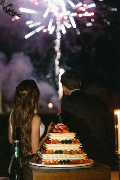 Bride and Groom cutting their cake while watching fireworks at their wedding reception in the Abbey of San Galgano in Tuscany Italy, photographed by Andrea-Marie Photography