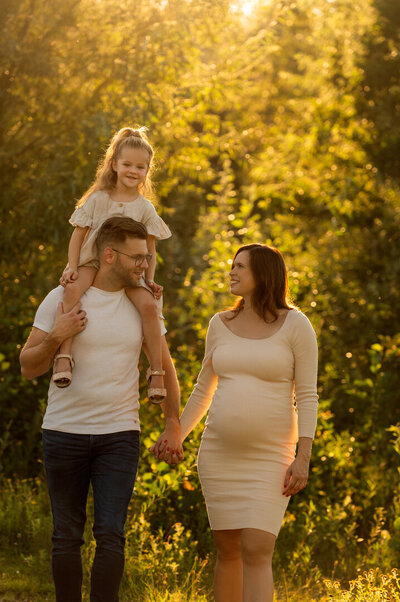 Gezinsshoot tijdens golden hour: dochter zit lachend op de rug van haar vader terwijl vader en moeder elkaar liefdevol aankijken – vastgelegd door Juliette Fotografie.
