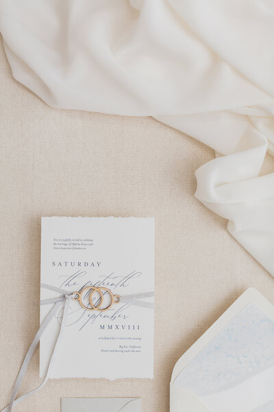 Wedding invite wrapped in ribbon with a dainty gold clasp.
