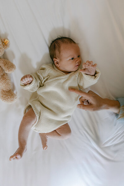 Family photo of a newborn baby wearing a knitwear jumpsuit laying on bedsheets