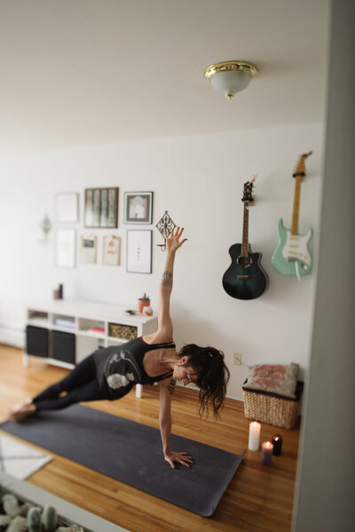 Miranda practicing side plank yoga pose in a cozy room decorated with guitars and candles, creating a calm and focused atmosphere.