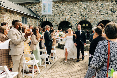 Couple walking down aisle after wedding ceremony with family and friends clapping and smiling