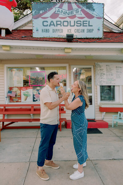 A couple holding ice cream cones out towards the other as they lick them 