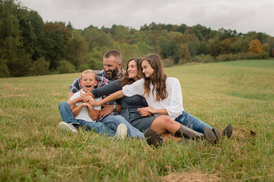 family of four sitting in grass tickle little borther