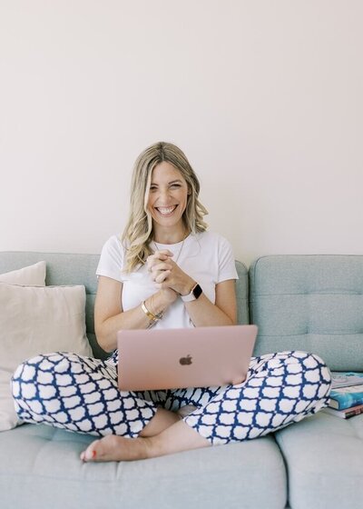 Branding session of a women hand clasped together, smiling, with a laptop on her lap.