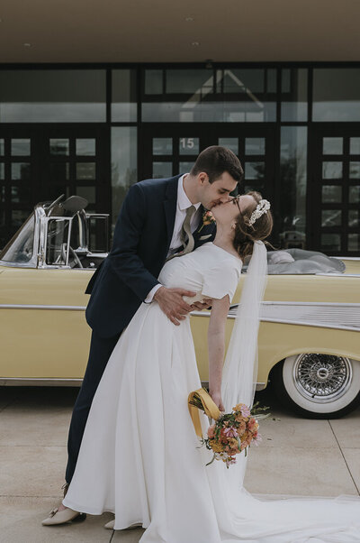bride and groom kissing in front of a vintage car