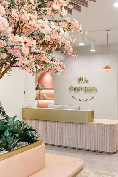 Beautiful pediatric dentist reception and waiting area in Andersonville, Chicago, Illinois. Mid-century modern colors and design are updated into a gorgeous office design, prominently featuring the Little Chompers logo in soft gold, behind the receptionist's desk.