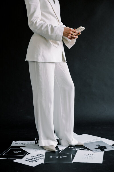 A woman standing on pieces of paper in a white suit on her phone 