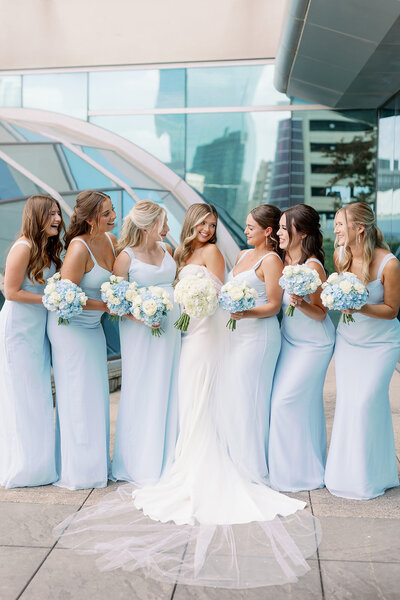 Bride and bridesmaids laughing with each other at omni hotel in Fort Worth with blue floral bouquets by Kortney Boyett Photography