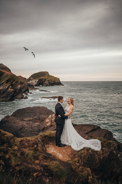 bride and groom embrace on the rocks by the ocean on their wedding day